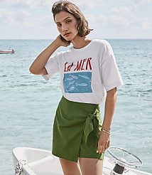 A woman in a white t-shirt and green skirt stands on a boat with the ocean and a distant boat in the background. carousel Product Image 1