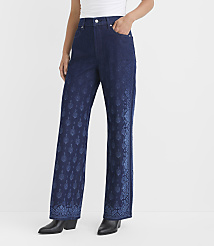 A person stands in dark blue flared jeans with a patterned design on the legs, against a plain white background. carousel Product Image 2