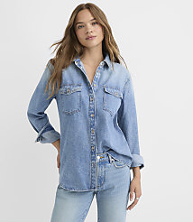 A young woman in a light blue denim shirt and jeans stands against a plain white background. carousel Product Image 1