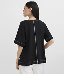 A woman in a black t-shirt with white stitching stands against a plain white background. carousel Product Image 3