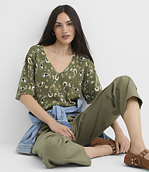 A woman in a paisley print top and olive green pants sits against a plain white background. carousel Product Image 1