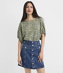 A woman in a green paisley-patterned top and a denim skirt stands against a plain white background. carousel Product Image 1