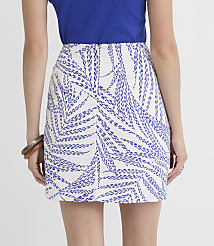 A woman in a blue top and a white skirt with blue palm leaf patterns stands against a plain white background. carousel Product Image 3
