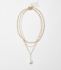 Three delicate gold necklaces, one with a single baroque pearl pendant, are arranged against a plain white background. carousel Product Image 1