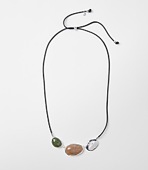 A black cord necklace with three polished stones&mdash;green, peach, and white&mdash;is laid out against a plain white background. carousel Product Image 1