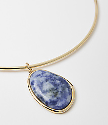 A gold choker necklace with a large, oval-shaped blue and white stone pendant hangs against a plain white background. carousel Product Image 2