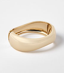 A gold-toned, abstractly shaped bracelet rests on a plain white background. carousel Product Image 1