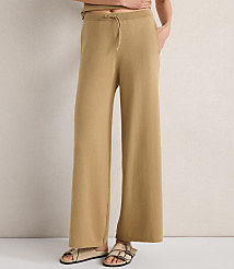 A person stands in tan wide-leg pants and sandals against a textured off-white background. carousel Product Image 2