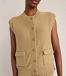 A close-up of a person wearing a tan knit vest with buttons and pockets is set against a plain, light-colored background. carousel Product Image 3