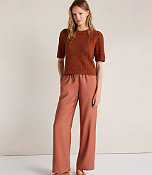 A woman in a rust-colored textured top and wide-leg rust pants stands against a textured cream background. carousel Product Image 2