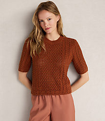 A woman in a brown knit top and pink pants stands against a textured gray background. carousel Product Image 1