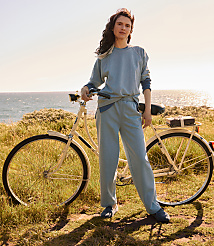 A woman in a light blue tracksuit stands with her bicycle on a grassy hill overlooking the ocean. carousel Product Image 5