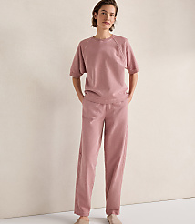 A woman in a pink loungewear set stands with her hands in her pockets against a plain, light-colored wall. carousel Product Image 1