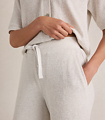 A person's hands are in the pockets of light-colored textured lounge pants, with a matching textured shirt visible above, against a plain, neutral background. carousel Product Image 3