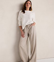 A woman in a white long-sleeved shirt and beige wide-leg pants stands against a textured cream wall. carousel Product Image 2