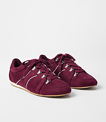 A pair of burgundy suede sneakers with white laces and silver eyelets rests on a white surface against a plain white background. carousel Product Image 1