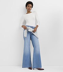 A woman in a white long-sleeved shirt and wide-leg jeans stands against a plain white background. carousel Product Image 1