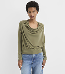 A woman in a green cowl-neck top and blue jeans stands against a plain white background. carousel Product Image 1