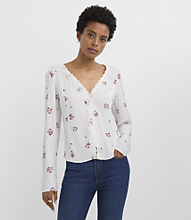 A woman in a white floral blouse and blue jeans stands against a plain white background. carousel Product Image 2