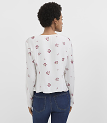 A woman in a white floral blouse and blue jeans stands against a plain white background. carousel Product Image 3