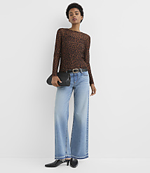 A woman in a leopard print top and wide-leg jeans stands against a plain white background, holding a black clutch. carousel Product Image 2