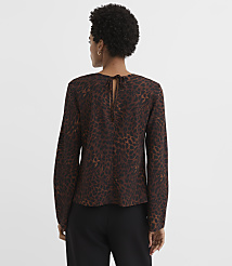A woman in a brown leopard-print blouse with a tie at the back stands against a plain, light brown background. carousel Product Image 3