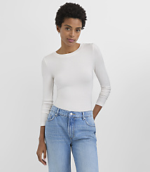 A woman in a white long-sleeved shirt and blue jeans stands against a plain white background. carousel Product Image 2