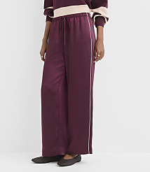 A person wearing burgundy satin wide-leg pants with a white stripe down the side stands against a plain white background. carousel Product Image 2