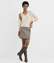 A woman in a cream cable-knit tank top, matching cardigan, and a brown plaid skirt stands against a plain white background. carousel Product Image 2