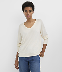 A woman in a cream v-neck sweater and blue jeans stands against a plain white background. carousel Product Image 1