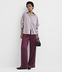 A woman in a striped shirt and burgundy pants stands against a plain white background, holding a small black bag. carousel Product Image 1