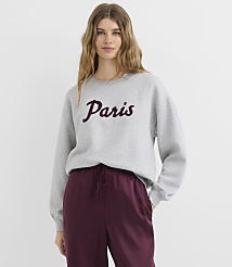 A young woman in a gray sweatshirt with "Paris" written on it stands against a plain white background. carousel Product Image 2