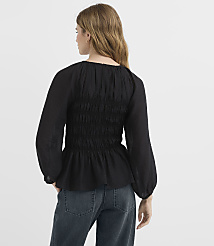 A woman in a black smocked blouse and jeans stands against a plain white background. carousel Product Image 3