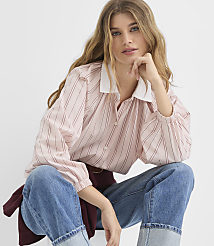 A woman with long blonde hair wearing a pink striped blouse and blue jeans poses against a plain white background. carousel Product Image 1