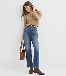 A woman in a tan cardigan and blue jeans stands against a plain white background, holding a brown purse. carousel Product Image 2