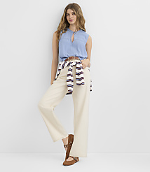 A woman in a light blue sleeveless top and cream-colored wide-leg pants stands against a plain white background, with a striped sweater tied around her waist. carousel Product Image 2