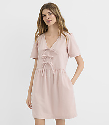 A woman in a pink dress with bow details stands against a plain white background. carousel Product Image 1