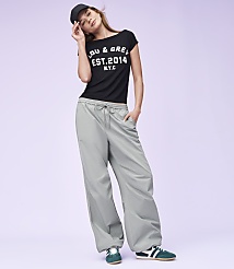 A woman in a black t-shirt and grey pants poses against a plain purple background. carousel Product Image 4