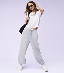 A woman in a white t-shirt and light blue sweatpants poses against a soft purple background. carousel Product Image 3