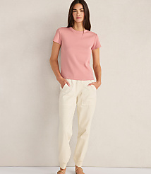 A woman in a pink t-shirt and cream pants stands against a textured, light-colored wall. carousel Product Image 2