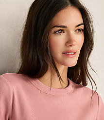 A woman with dark hair and light skin wears a pink ribbed shirt in the foreground, with a textured, light-colored wall in the background. carousel Product Image 3