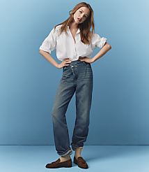 A young woman in a white shirt and blue jeans stands with her hands on her hips against a solid blue background. carousel Product Image 6