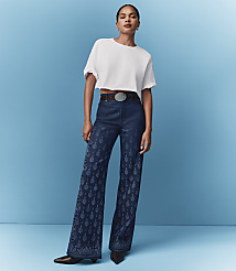 A woman in a white crop top and patterned flared jeans stands against a solid blue background. carousel Product Image 6