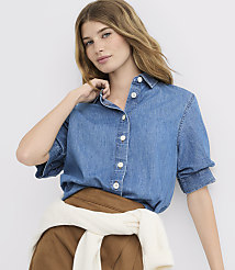 A young woman in a denim shirt and brown pants, with a white sweater tied around her waist, poses against a plain white background. carousel Product Image 1