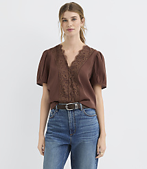 A woman in a brown lace-trimmed blouse and blue jeans stands against a plain white background. carousel Product Image 1