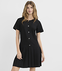 A young woman in a black dress with a pleated skirt stands against a plain white background. carousel Product Image 1
