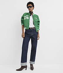 A woman in a green bomber jacket and dark jeans stands against a plain white background. carousel Product Image 1