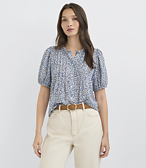 A woman in a floral blouse and cream pants stands against a plain white background. carousel Product Image 1