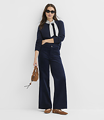 A woman in a navy sweater and wide-leg corduroy pants stands against a plain white background, holding a small brown purse. carousel Product Image 1