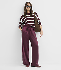A woman in a striped sweater and burgundy satin pants stands against a plain white background, carrying a brown suede bag. carousel Product Image 2